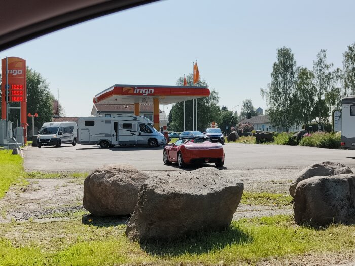 Bensinmack med flera bilar och husbilar som köar för att tanka, med stenar i förgrunden och Ingo-skylt i bakgrunden.