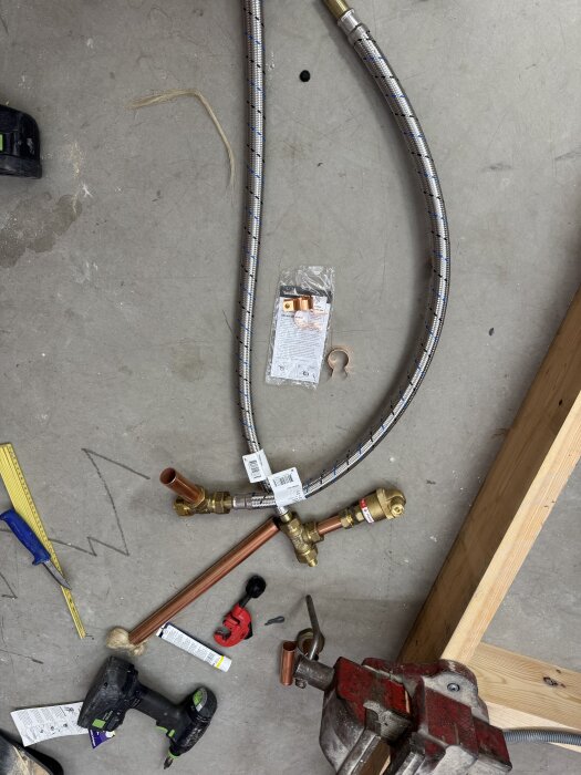 Verktyg och material för frikyla installation på betonggolv, inklusive pressmaskin, kopparrör och slang.