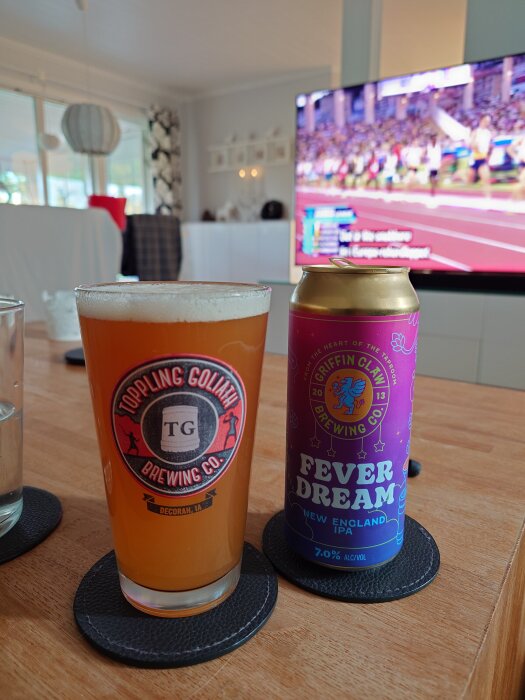Glas med öl och en burk Fever Dream New England IPA på ett bord, i bakgrunden visas en sportkanal på TV:n.