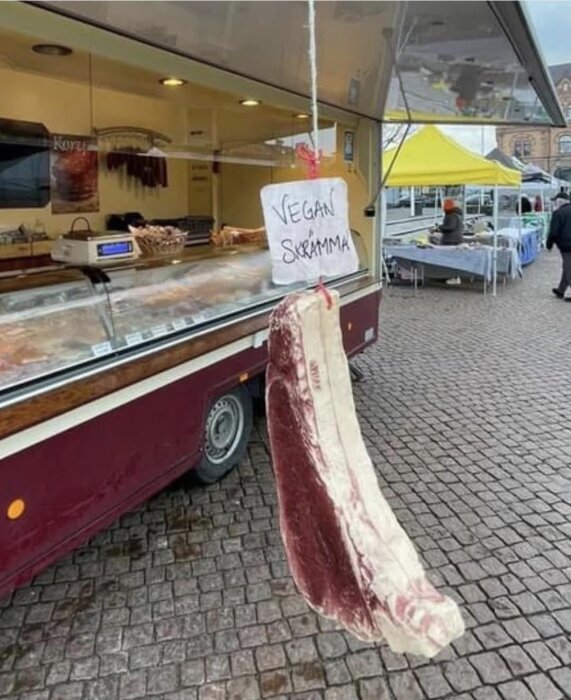 En köttbit hängd utanför en matvagn på torget med en skylt som säger "Vegan skrämma".