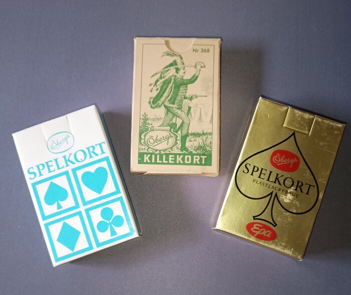 Tre förpackningar av Öbergs spelkort, inklusive Killekort och Spelkort, med retrodesign.