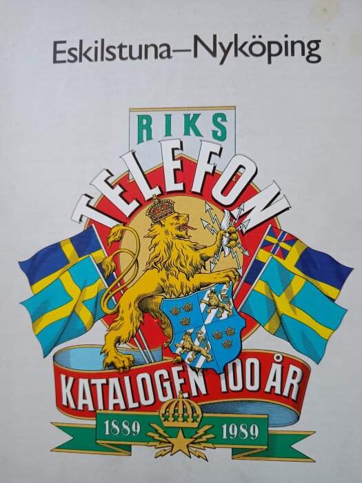 Omslag för Rikstelefonkatalogens 100-årsjubileum 1889–1989 med svenska flaggor, ett lejon och texten Eskilstuna–Nyköping.