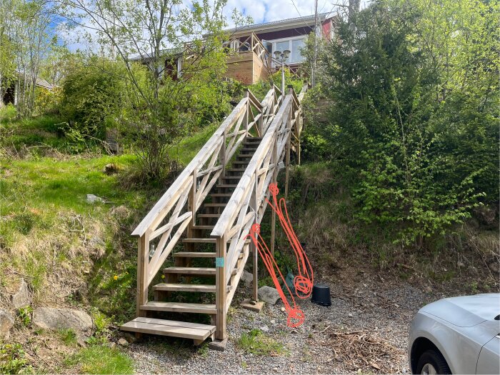Trätrappa på en kulle med stödlinjer ritade, omgiven av grönska. Trappan är fast förankrad upptill men ligger löst på marken.