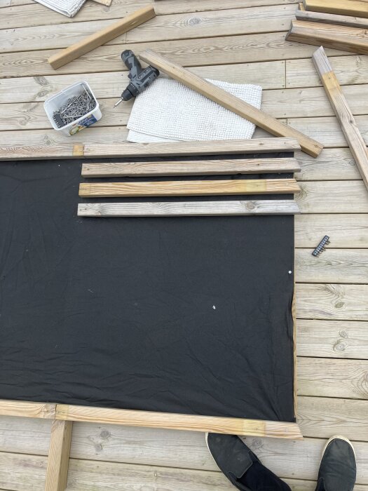 Verktyg och material för plankbygge, inklusive träreglar, tygduk, skruvar, borrmaskin och fötter på en trätrall.