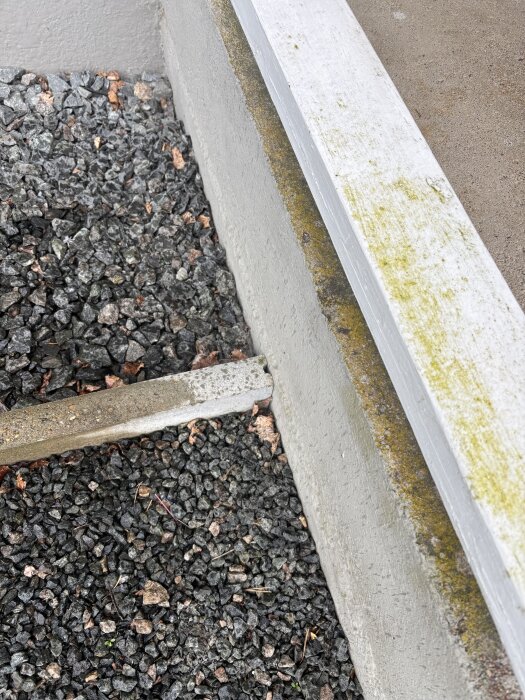 Entré med betongtrappa och ojämn gavel, synlig grusad yta och målad kant, delvis täckt av smuts och mossa, i behov av renovering.