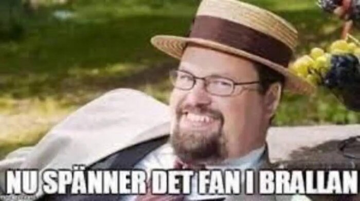En man med hatt och glasögon ler i en park. Texten "NU SPÄNNER DET FAN I BRALLAN" är över bilden.