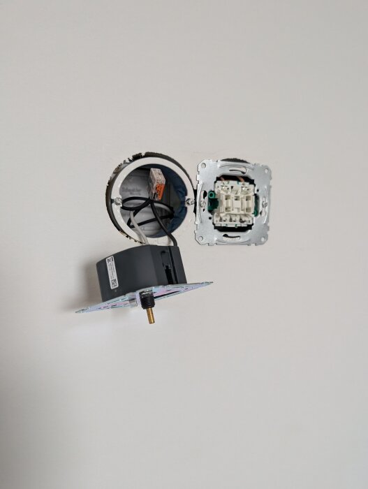 Öppnad dimmer med exponerade kablar och elkomponenter i en vägg, potentiell orsak till bränd plastlukt när en lampa flyttas till annat rum.