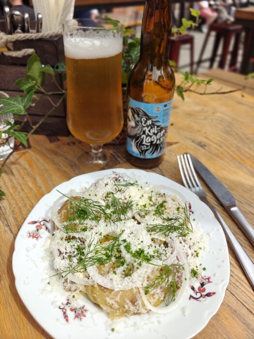 Silltallrik med lök och dill, serverad med ölflaska och glas på träbord.