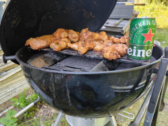 Grill med marinerad kyckling och fläskfilé samt en ölburk placerad bredvid.