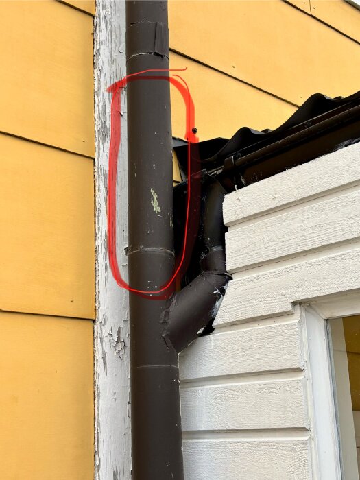 Nedre del av ett stuprör intill en husvägg markerad med rött, med en sektion av takränna och gula paneler i bakgrunden.