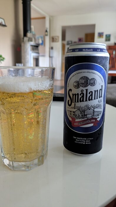 Glas med öl bredvid en burk Småland mellanöl på ett bord.