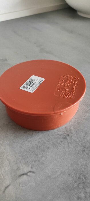 Röd plastlock från Ostendorf KG med etikett, placerad på en grå yta.