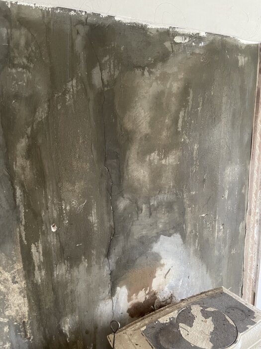 Vägg med putsrester och spår av olika bruk, med en modern kamin i nederkanten.