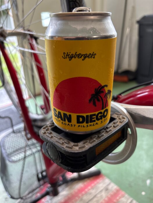 En ölburk av märket Stigbergets San Diego placerad på en cykelpedal i ett garage.