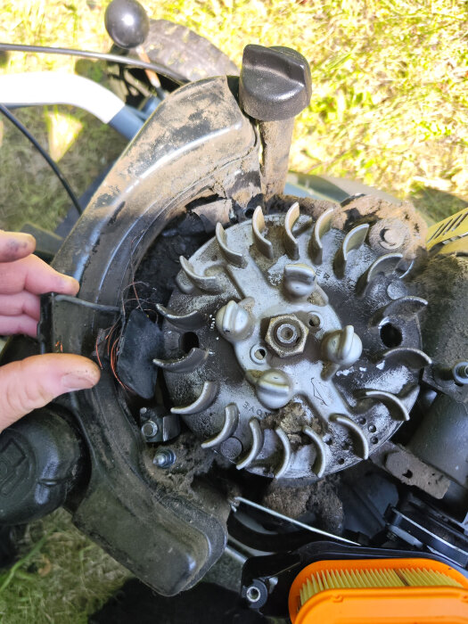 Närbild på en trasig växelströmsgenerator på en gräsklippare. Generatorn har lossnat från motorn och gängorna är skadade.