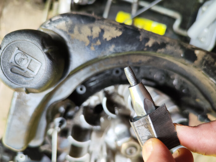 Närbild av trasig växelströmsgenerator på en Stiga Multiclipper, delvis borttagen från fäste, omgiven av motor- och metallkomponenter.