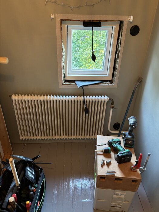 Bygge med nytt fönster ovanför element, verktyg på låda och verktygsväska på golv.