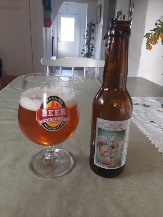 Flaska och glas med Fulltofta Zeehphyra Dubbel IPA på ett bord, omgiven av heminredning.
