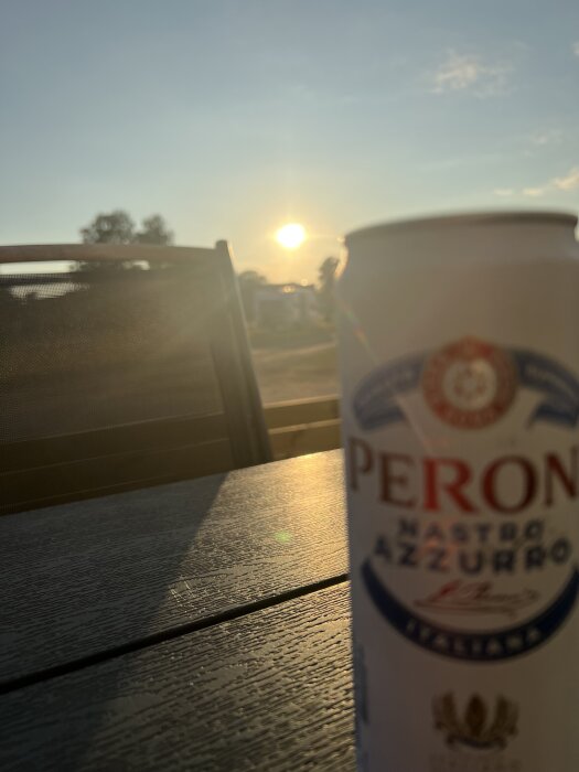 Solnedgång över ett bord med en suddig ölburk i förgrunden.