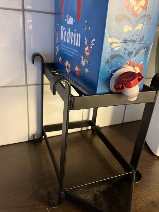 Bag in box med rödvin på ett svart metallstativ i kök.