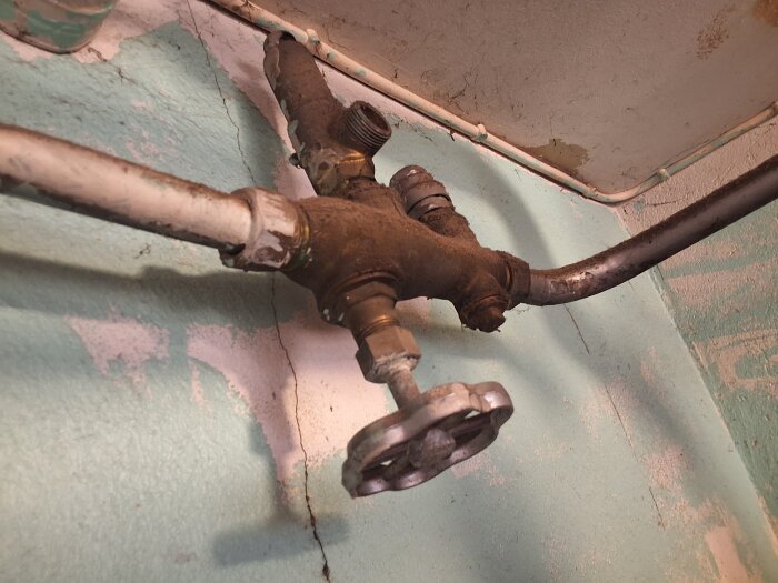 Rostig vattenventil från 1963 i pannrum med ansluten kopparrörledning, omgiven av svagt grönmålad vägg.