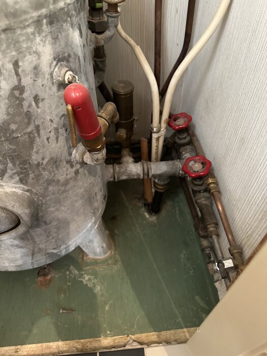 VVS-installation med en hydrofor, flera rör och ventiler, inklusive en röd tömningskran och anslutningar till vattenberedare.