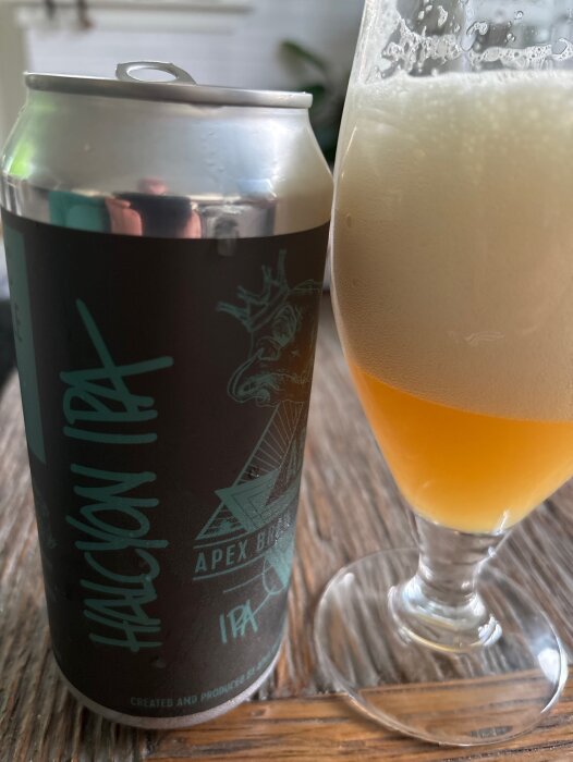 Apex Halcoyon IPA burk och glas med öl och skummig yta på ett träbord.