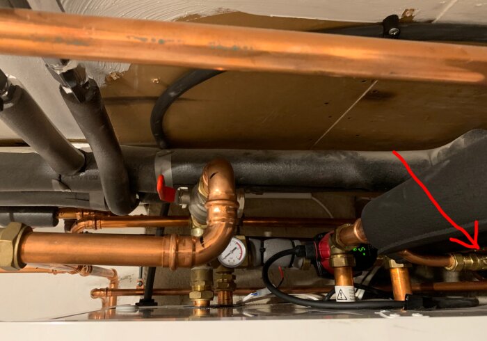 Kopparrör och ventiler, eventuellt en del av ett VVS-system, med en röd pil som pekar mot en påfyllningsventil.