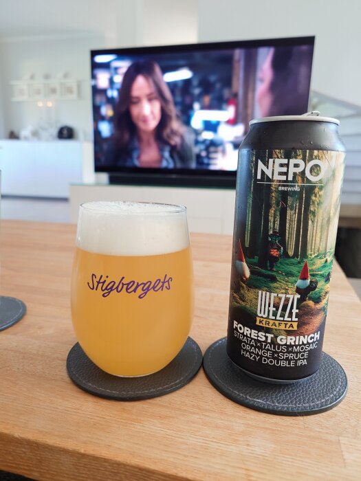 En glas öl på ett bord bredvid en burk med etikett "Nerobryggeri Forest Grinch IPA". En TV syns i bakgrunden.