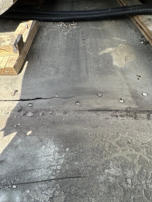 Underlagspapp vid takfot med hål och spår av vatteninträngning, träbalkar synliga på sidan, tagen från tak med låg lutning.