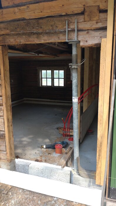 Renovering av en sommarstuga med öppet träarbete, provisorisk stöttning och synliga rörledningar i en oinredd utbyggnad.