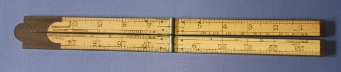 Äldre vikbar tumstock med mässingsbeslag och markerade mått, liggande på en blå bakgrund.