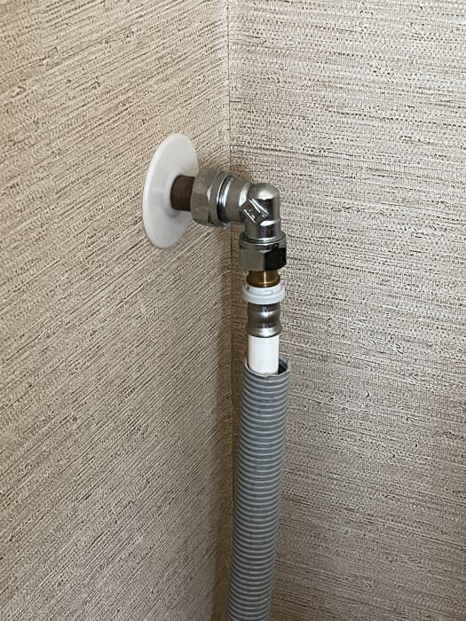 Ett kopparrör med en metallkoppling syns i ett hörn av ett rum. En plastslang är ansluten till kopplingen.