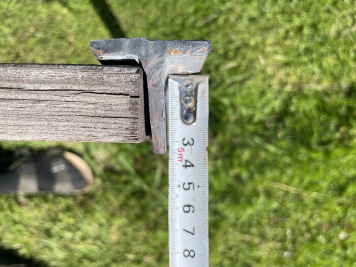 Gammalt staket med sprickor, mätt med måttband mot grön gräsmatta.