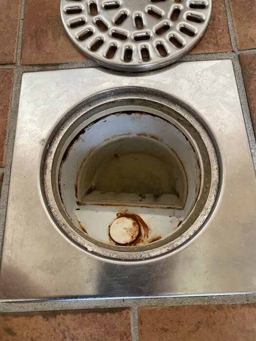 Äldre golvbrunn med rost och liten glipa mellan brunn och ring i ett badrum.