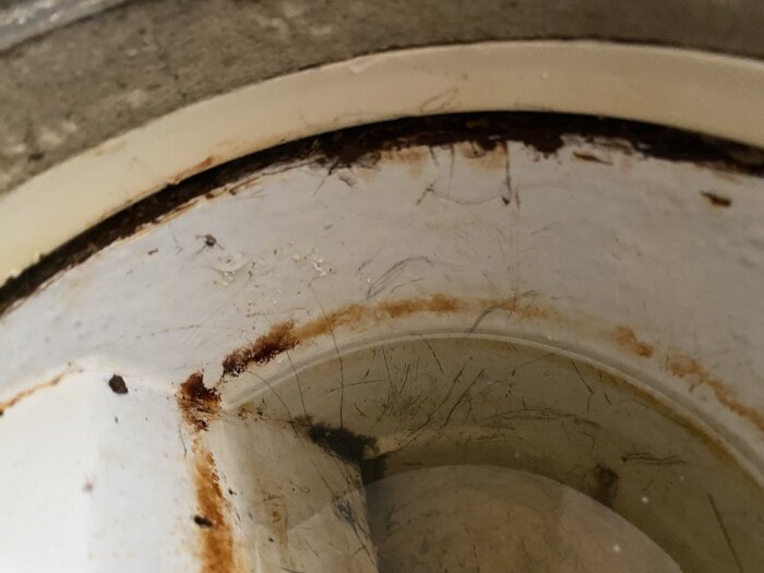Äldre golvbrunn med rost och en glipa mellan brunn och ring i ett badrum.
