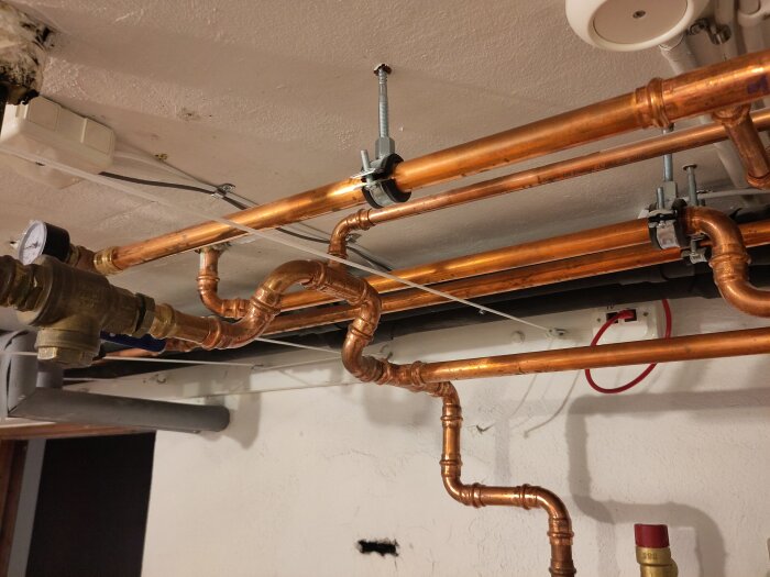 Kopparrör i källartaket med nätverkskabel och röd patchkabel kopplad till uttag för värmepump.