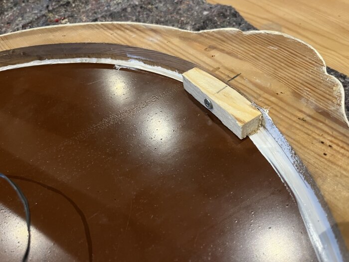 Träram med spegel, fixad med fogmassa längs kanterna och förstärkt med träbitar på baksidan, inomhus på ett arbetsbord.