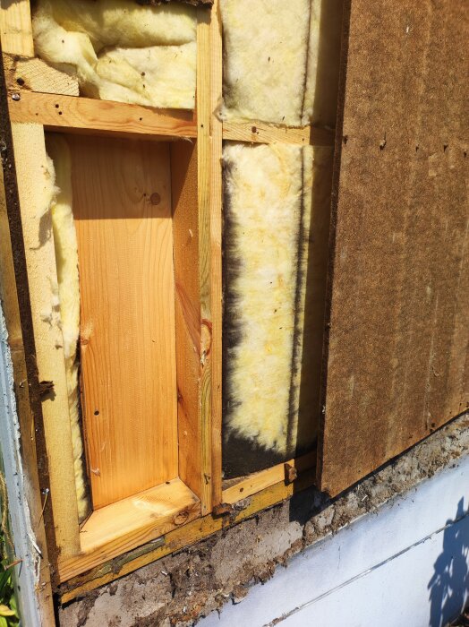 Bild av en husvägg under renovering, visar träreglar, gul isolering och asfaboard.
