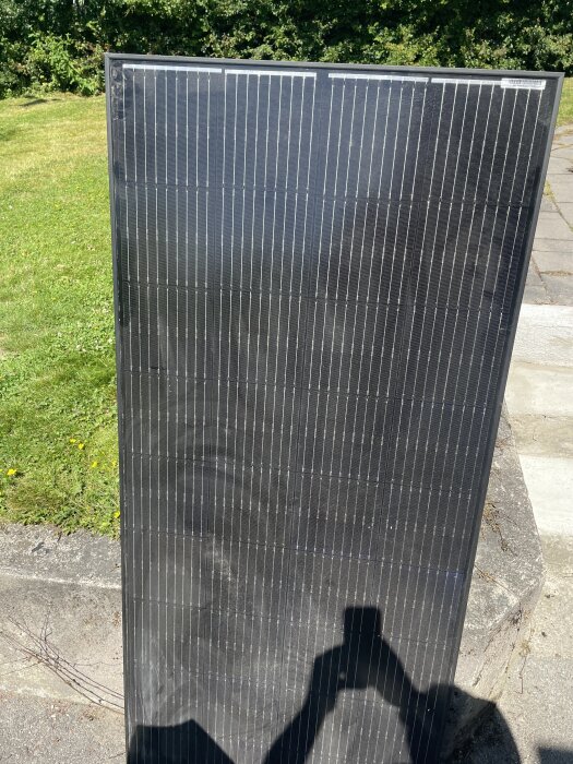 Solpanel lutad mot en betongyta utomhus, delvis skugglagd av en fotograf.