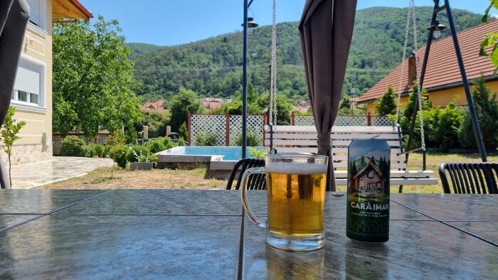 Ölglas och burk på ett bord utomhus med en pool i bakgrunden.