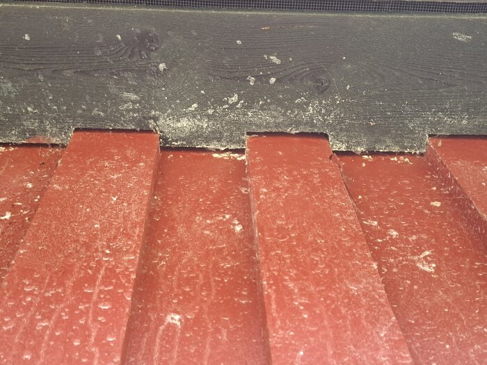 Rött plåttak med slitage och svart panel i vinkeln mellan takfot och fasad, från en gammal träkåk byggd 1979. Inga tydliga tecken på läckage syns.