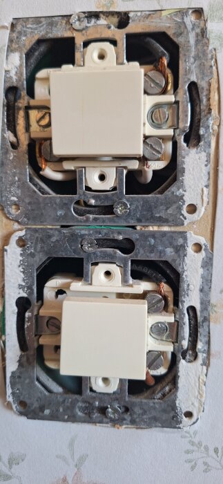 Två strömbrytare med synliga ledningar och skruvanslutningar; brun, svart och blå ledning kan ses för anslutningar respektive jordning.