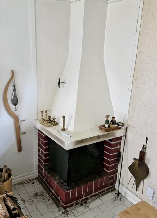Öppen spis med vit skorsten och röd tegelbas, dekorerad med ljusstakar och figurer i köksmiljö. Golvet har ljusa kakelplattor.