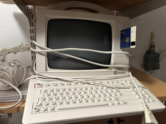 En vit Teleguide-terminal med tangentbord, kablar och ett kort instoppat på sidan, placerad på en hylla.