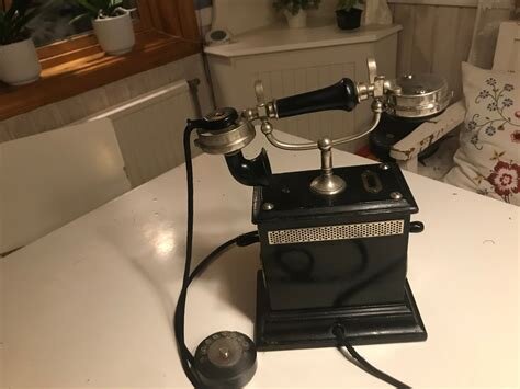 Svart gammaldags telefon med vev och två lurar, placerad på ett bord i ett rum.