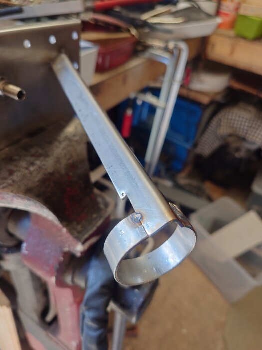 Metallfäste svetsat på stålrör, synligt inuti ett verkstadsutrymme med verktyg och utrustning i bakgrunden.