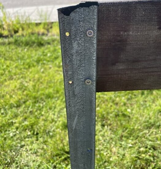 Äldre staketstolpe med skruvar och träbräda, på en gräsmatta, där virke behöver fästas på nytt.