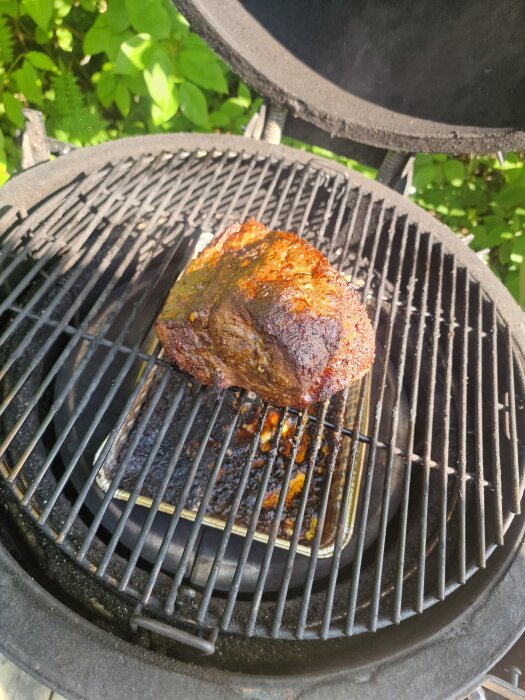 Pulled pork halvvägs på en grill, med kolbriketter och droppbricka under köttet.