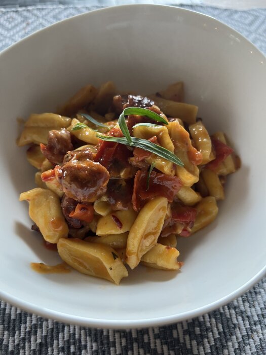 Hemlagad salsicciapasta med chili, vitlök och tomat, toppad med västerbottenost och färska örter i en vit skål.